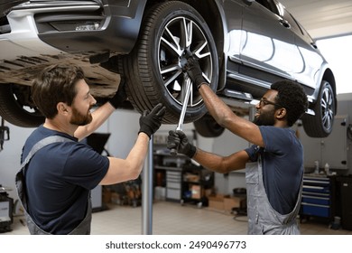 Mechanics performing tire maintenance on car in auto repair shop. Teamwork and cooperation in automotive service. Professional technicians using tools for car repair and maintenance. - Powered by Shutterstock