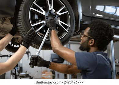 Mechanics using tools to fix car wheel in auto repair shop. Teamwork in automotive maintenance and tire repair. Close-up of workers' hands and tools. - Powered by Shutterstock