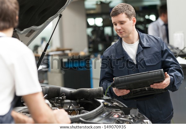 Mechanics at work shop. Two confident auto mechanics\
working at the repair\
shop