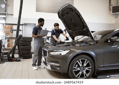 Mechanics working on car maintenance in modern auto repair shop, using laptop and tools. Auto repair, service check, and team collaboration displayed. - Powered by Shutterstock