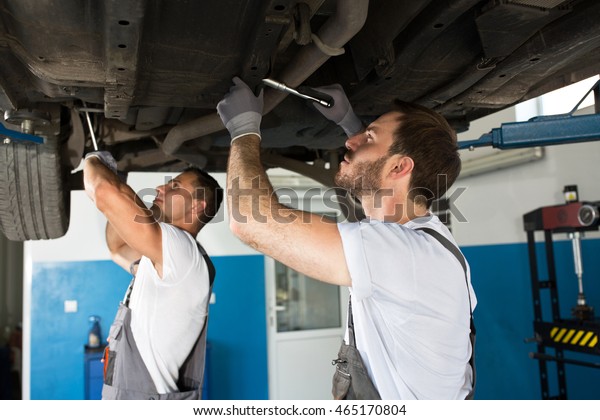 Mechanics working together under the car with a tools\
and repair car