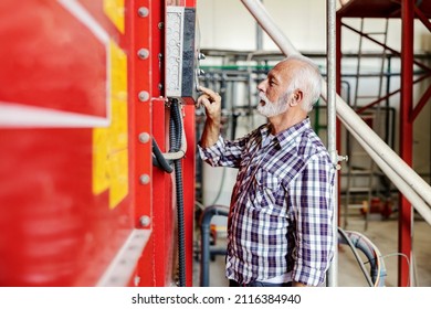 Mechanization And Industrialization In The Factory. A Senior Factory Worker Standing Next To A Dashboard With A Start Button And Pressing It To Start A Machine.