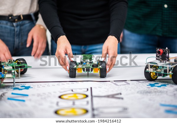A mechatronic\
robot with artificial intelligence on wheels thrown by a woman\'s\
hands on a table with a\
canvas.