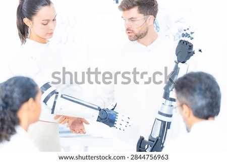 Mechatronics engineering team, an engineer setting the fingers of a tall robotic arm into position while a colleague follows the linkage back toward the shoulder.