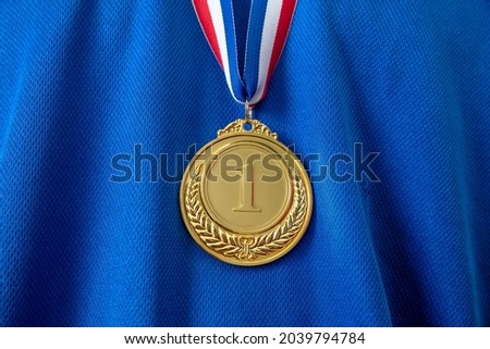 Medal gold, Winner prize award hanging with red blue color ribbon on athlete chest. Golden trophy in sport for first place champion on blue color shirt background