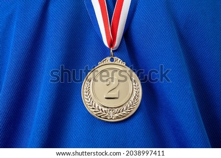 Medal silver. Winner prize award hanging with red blue color ribbon on athlete chest. Trophy in sport for second place champion on blue color shirt background