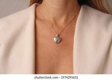Medallion pendant in shape of heart made of silver on chain hangs around neck, on chest of a young girl. Love and romance, beautiful gift heart medallion pendant, beautiful jewelry on the girl.