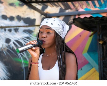 Medellin, Colombia - September 9 2021: Black Female Rapper Dressed In White With Bandana Singing In Microphone In The Comuna 13, Touristic Artistic Urban Attraction Cultural Historical Neighborhood