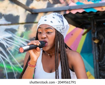 Medellin, Colombia - September 9 2021: Black Female Rapper Dressed In White With Bandana Singing In Microphone In The Comuna 13, Touristic Artistic Urban Attraction Cultural Historical Neighborhood