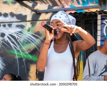 Medellin, Colombia - September 9 2021: Black Female Rapper Dressed In White With Bandana Singing In Microphone In The Comuna 13, Touristic Artistic Urban Attraction Cultural Historical Neighborhood