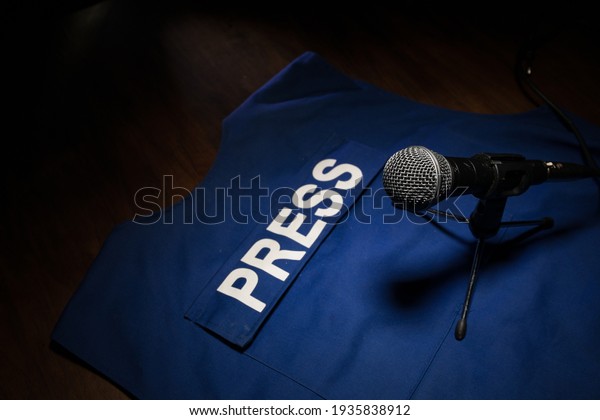 Media Journalism Global\
Daily News Content Concept. Blue journalist (press) vest in dark\
with backlight and fog. Media microphone on journalist vest.\
Selective focus