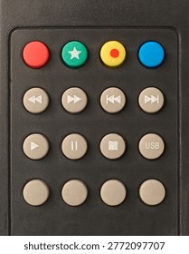 media playback and function buttons on matte black plastic remote control, red green yellow blue and grey rubber buttons with white symbols, top view closeup in full frame background