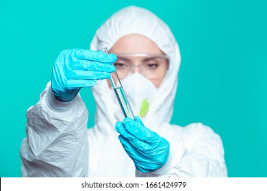 A medic girl in a protective suit, a respirator and glasses studies the drug coronavirus in a glass test tube.