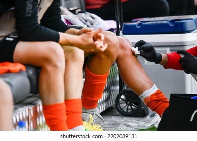 A Medic Treats The Wounds On The Leg Of A Football Player Sitting On The Bench