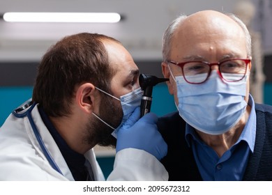 Medic Using Otoscope To Do Ear Checkup On Senior Man, Doing Otolaryngology Consultation With Patient. Doctor With Face Mask Examining Infection To Give Prescription Treatment. Close Up