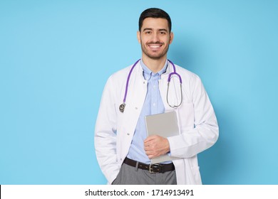 Medic In White Robe, Looking Straight At Camera With Positive Smile, Holding Tablet Computer Next To Chest While Working In Hospital, Isolated On Blue Background