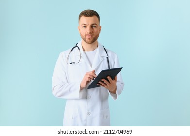 Medic In White Robe, Looking Straight At Camera With Positive Smile, Holding Tablet Computer Next To Chest While Working In Hospital, Isolated On Blue Background