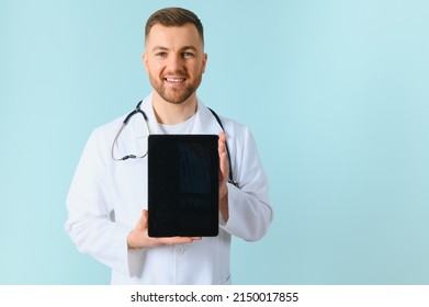 Medic In White Robe, Looking Straight At Camera With Positive Smile, Holding Tablet Computer Next To Chest While Working In Hospital, Isolated On Blue Background