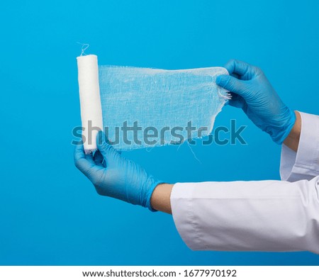 medic woman in white coat holds a twisted gauze bandage, blue background, medical item for bandaging human limbs