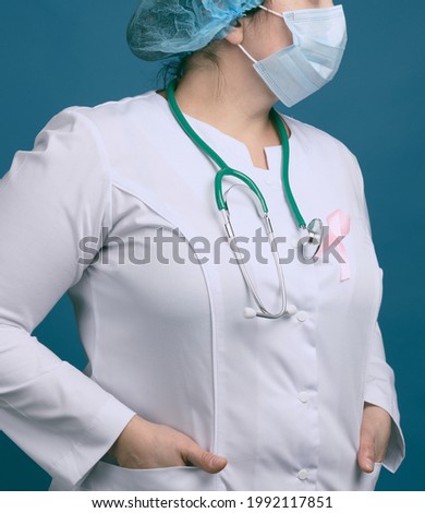 medic woman in white coat, pink ribbon pinned to the robe, symbol of the fight against breast cancer in October, blue background