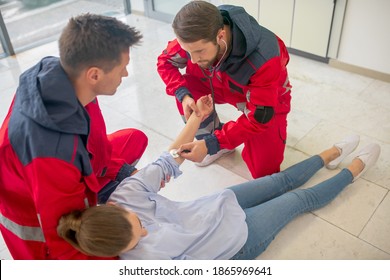 Medical aid. Two medical workers in red uniform halping a faint woman - Shutterstock ID 1865969641