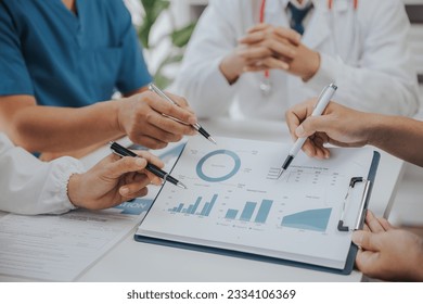 Medical analysts and physicians consult documents on graphs, data and charts in a hospital conference room. - Powered by Shutterstock