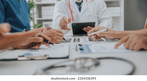 Medical analysts and physicians consult documents on graphs, data and charts in a hospital conference room. - Powered by Shutterstock