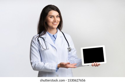 Medical App. Female Doctor Showing Digital Tablet Blank Screen Standing On Gray Background. Studio Shot, Mockup