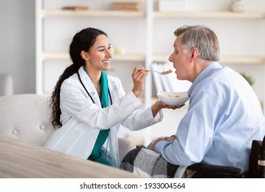 Medical assistance for elderly people with disabilities. Young nurse feeding senior handicapped man in wheelchair at home. Older male patient eating breakfast with caregiver's help - Powered by Shutterstock