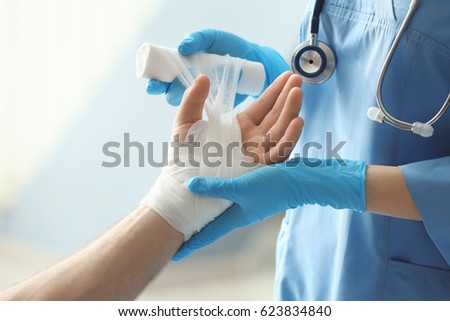 Medical assistant applying bandage onto patient's hand in clinic, closeup