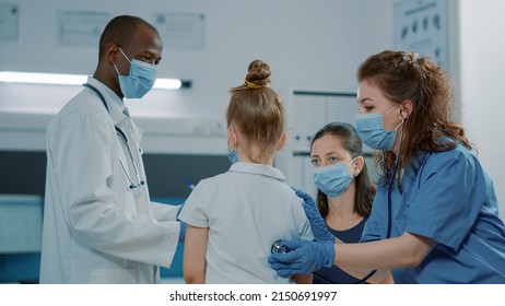 Medical assistant consulting small kid with stethoscope in office. Woman nurse in uniform checking pulse and heartbeat, finding health care diagnosis during covid 19 pandemic.