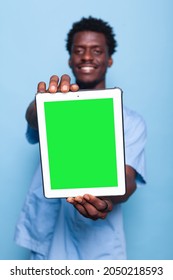 Medical Assistant Holding Digital Tablet With Vertical Green Screen. Man Working As Nurse In Uniform Smiling, Showing Gadget Display With Chroma Key And Mockup Template On Isolated Background