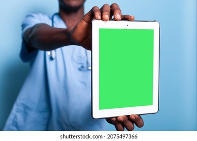 Medical Assistant Holding Digital Tablet With Green Screen. Man Working As Healthcare Nurse In Uniform Showing Gadget Display With Chroma Key And Mockup Template On Isolated Background