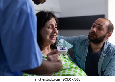 Medical Assistant Holding Hand Of Pregnant Woman Sitting In Hospital Ward Bed. Young Husband Supporting Wife Getting Ready For Labor And Childbirth At Medical Clinic While Nurse Assisting