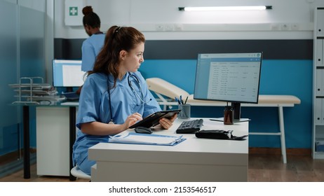 Medical Assistant Typing On Tablet Screen And Checking Computer For Appointment In Doctors Office. Nurse Looking At Monitor While Using Modern Gadget For Healthcare Checkup Visit.