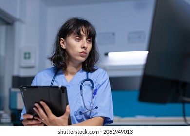 Medical assistant using digital tablet with touch screen for healthcare. Woman nurse holding device and analyzing computer display, working late at night. Specialist with gadget - Shutterstock ID 2061949013