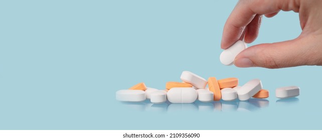 Medical background. Hand holds one of many capsule tablets or pills on blue table. Close up. Healthcare pharmacy and medicine concept with copy space Painkillers or prescription drugs consumption