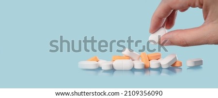 Medical background. Hand holds one of many capsule tablets or pills on blue table. Close up. Healthcare pharmacy and medicine concept with copy space Painkillers or prescription drugs consumption