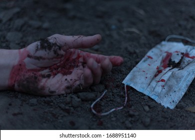 A Medical Bloodied Mask Lies On The Ground With A Bloody Hand Reaching Out. The Concept Of Coronavirus And The Apocalypse Resulting From This Disease Has Spread Throughout The World. Horror.