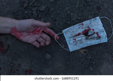 A Medical Bloodied Mask Lies On The Ground With A Bloody Hand Reaching Out. The Concept Of Coronavirus And The Apocalypse Resulting From This Disease Has Spread Throughout The World. Horror.