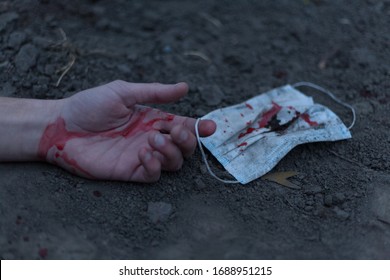 A Medical Bloodied Mask Lies On The Ground With A Bloody Hand Reaching Out. The Concept Of Coronavirus And The Apocalypse Resulting From This Disease Has Spread Throughout The World. Horror.