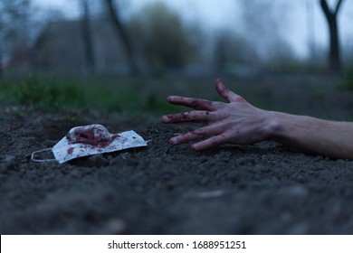 A Medical Bloodied Mask Lies On The Ground With A Bloody Hand Reaching Out. The Concept Of Coronavirus And The Apocalypse Resulting From This Disease Has Spread Throughout The World. Horror.