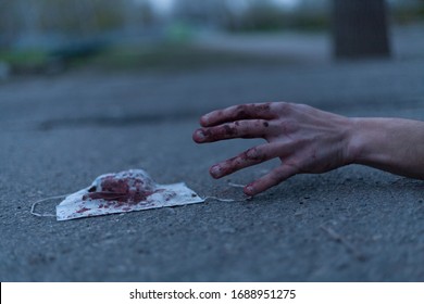 A Medical Bloodied Mask Lies On The Ground With A Bloody Hand Reaching Out. The Concept Of Coronavirus And The Apocalypse Resulting From This Disease Has Spread Throughout The World. Horror.