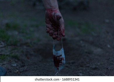 A Medical Bloodied Mask Lies On The Ground With A Bloody Hand Reaching Out. The Concept Of Coronavirus And The Apocalypse Resulting From This Disease Has Spread Throughout The World. Horror.