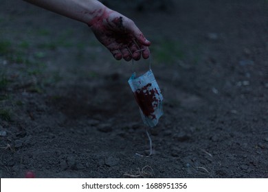 A Medical Bloodied Mask Lies On The Ground With A Bloody Hand Reaching Out. The Concept Of Coronavirus And The Apocalypse Resulting From This Disease Has Spread Throughout The World. Horror.