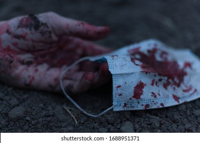 A Medical Bloodied Mask Lies On The Ground With A Bloody Hand Reaching Out. The Concept Of Coronavirus And The Apocalypse Resulting From This Disease Has Spread Throughout The World. Horror.