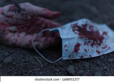 A Medical Bloodied Mask Lies On The Ground With A Bloody Hand Reaching Out. The Concept Of Coronavirus And The Apocalypse Resulting From This Disease Has Spread Throughout The World. Horror.