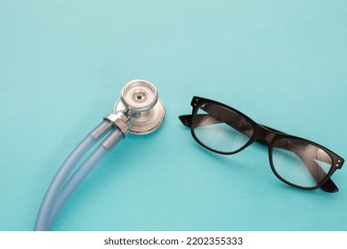 Medical Blu Stethoscope And Black Spectacles On Blu Background. Simply Minimal Design With Medicine Equipment Doctor Stethoscope And Classic Glasses , Closeup. Health Care Concept.