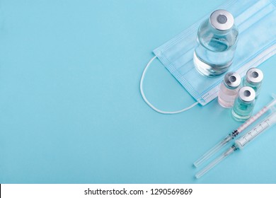 Medical bottle, vials, syringes and face mask on blue background with copy space. Vaccination session and immunity improvement.