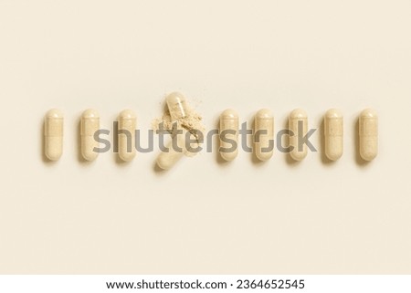 Medical capsules in a line with one opened to show beige powder on light beige top view. Preventive medicine and healthcare, dietary supplements and vitamins